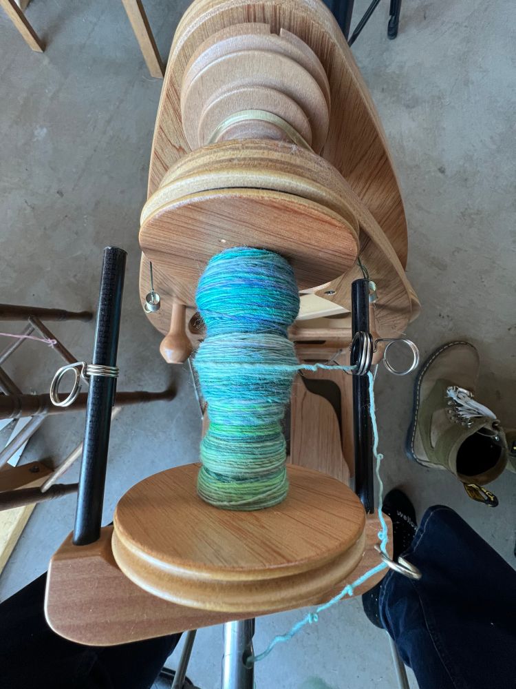A spinning wheel with brightly colored wool yarn on it. 