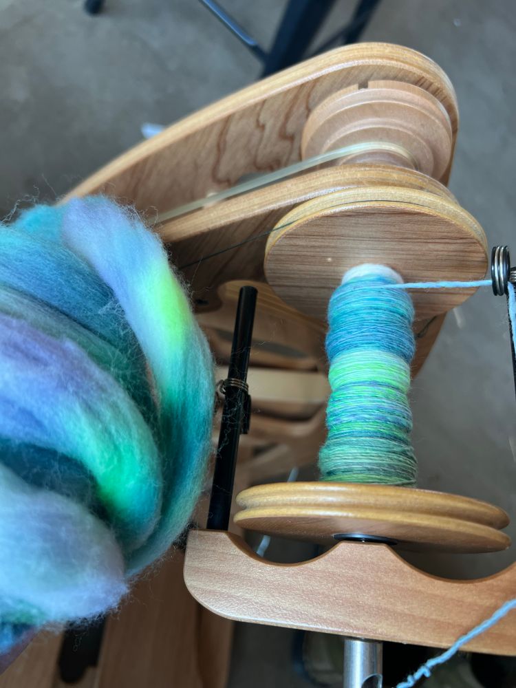 A spinning wheel with brightly colored wool and yarn on it. 