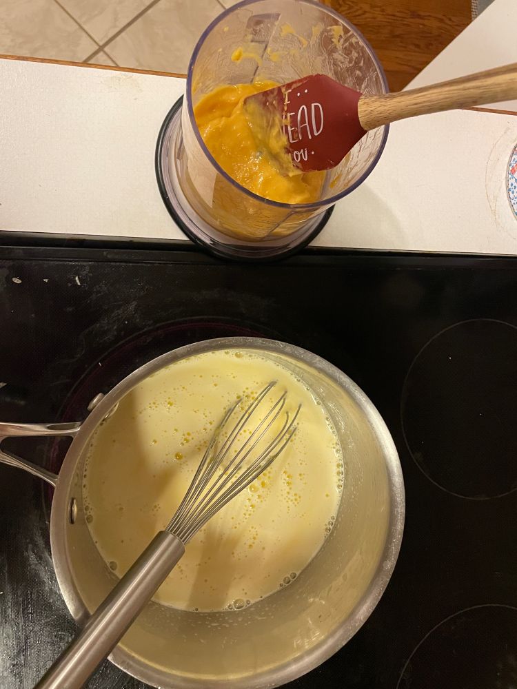 Top-down photo of a batch of pastry cream cooking in a pot with yellow pawpaw puree in a vessel beside it