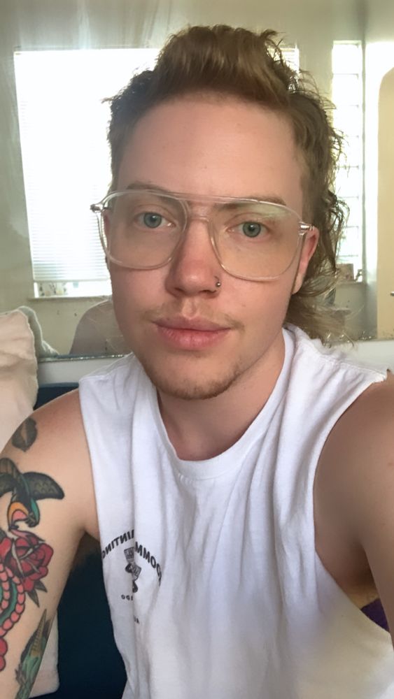 Gion, a red headed trans guy in a white muscle shirt 