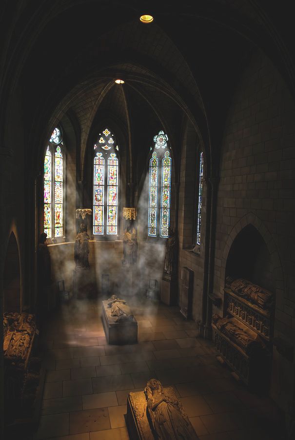 Golden rays of light pour through the intricate stained glass windows, casting a vibrant mosaic of colors upon the scene below at the MET Cloisters in the heart of New York City.