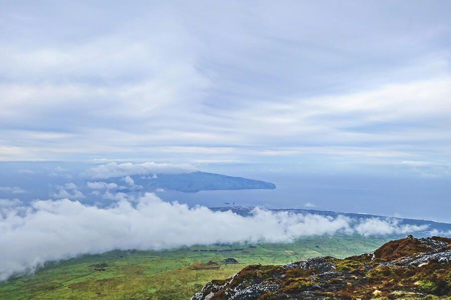 The enchanting Faial Island in the Azores Islands emerges from the vastness of the Atlantic Ocean, as seen from the ascension up Mount Pico on Pico Island.