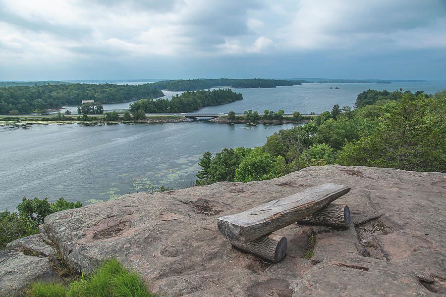 A lone, empty bench awaits weary hikers at the top of a trail in 1000 Islands National Park, Ontario, overlooking Landon Bay and the St. Lawrence River on a gloomy day.