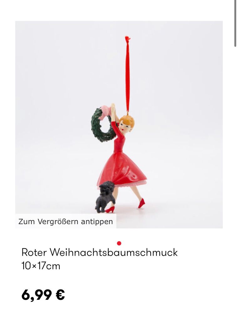 ein weihnachtsbaumschmuck in form einer frau im kleid, die einen kranz aufhängt und ein kleiner schwarzer hund zieht an ihrem rock