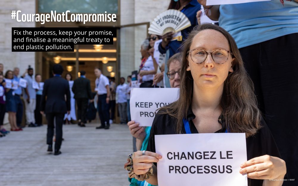 Vor dem Eingang des UN-Gebäudes in Genf stehen Menschen in einer stillen Protestreihe. Im Vordergrund hält unsere Kollegin Hanna Eberhard ein Schild mit der Aufschrift „CHANGEZ LE PROCESSUS“. Dahinter sind weitere Personen mit Schildern wie „KEEP YOUR PROMISE“ zu sehen. Links im Bild ist ein Banner mit dem Text „#CourageNotCompromise – Fix the process, keep your promise, and finalise a meaningful treaty to end plastic pollution“ eingeblendet.