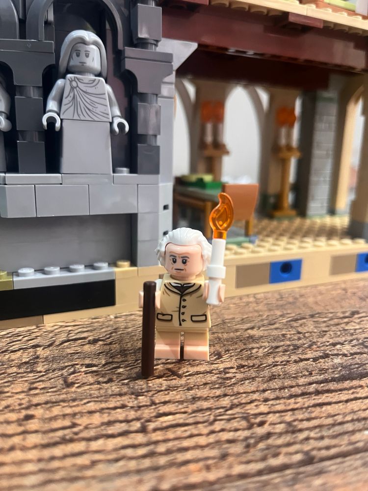 Lego Rivendell set. Bilbo minifigure in the foreground holding a cane and a candle. 
