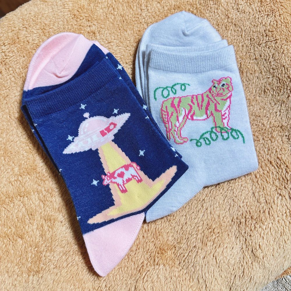 真新しい2枚の靴下の写真　エイリアンに攫われる牛の柄（左）黄緑とピンクの虎の柄（右）