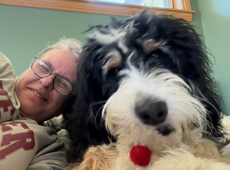 Corinne lays head to head with her dog, smiling