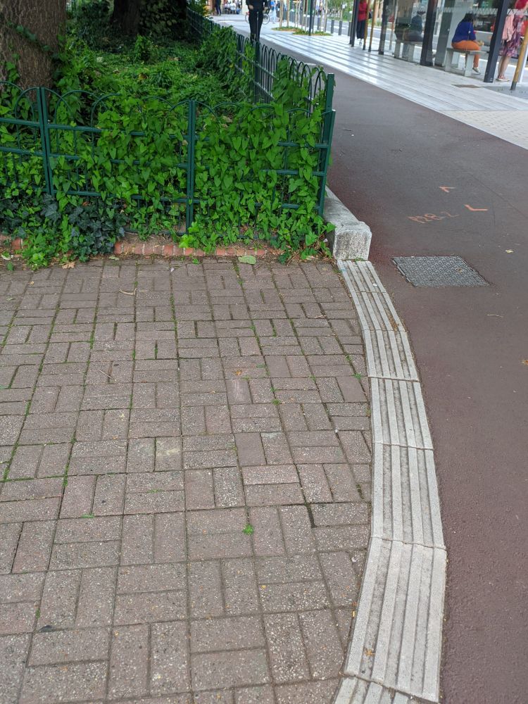 Autre côté du square par rapport à la photo précédente. La bande de guidage aboutit sur la bordure au pied de la clôture du parc.