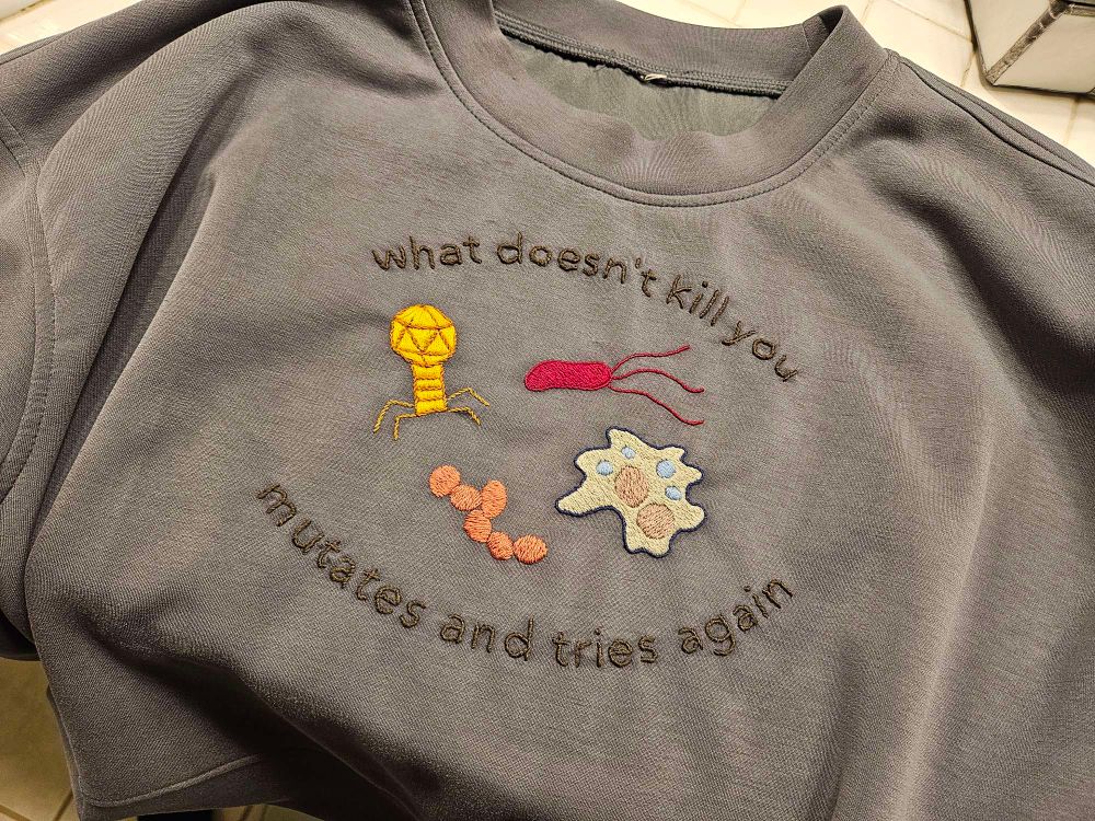 Photo of a sweater with the embroidery "what doesn't kill you mutates and tries again" with images of 4 microbes