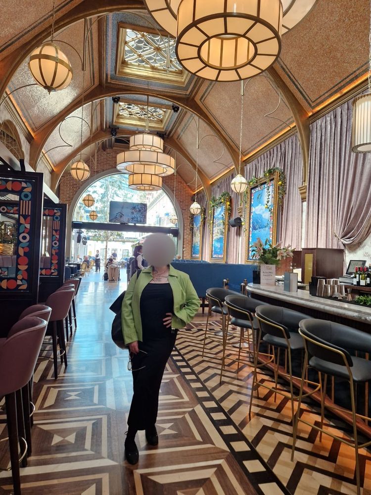 Mistress Jamie stands among the beautiful decor of cafe en seine, in a full length photo, she poses in her lime green leather jacket, black long body con dress and ballerina pumps. Posed with her hand on her hip.