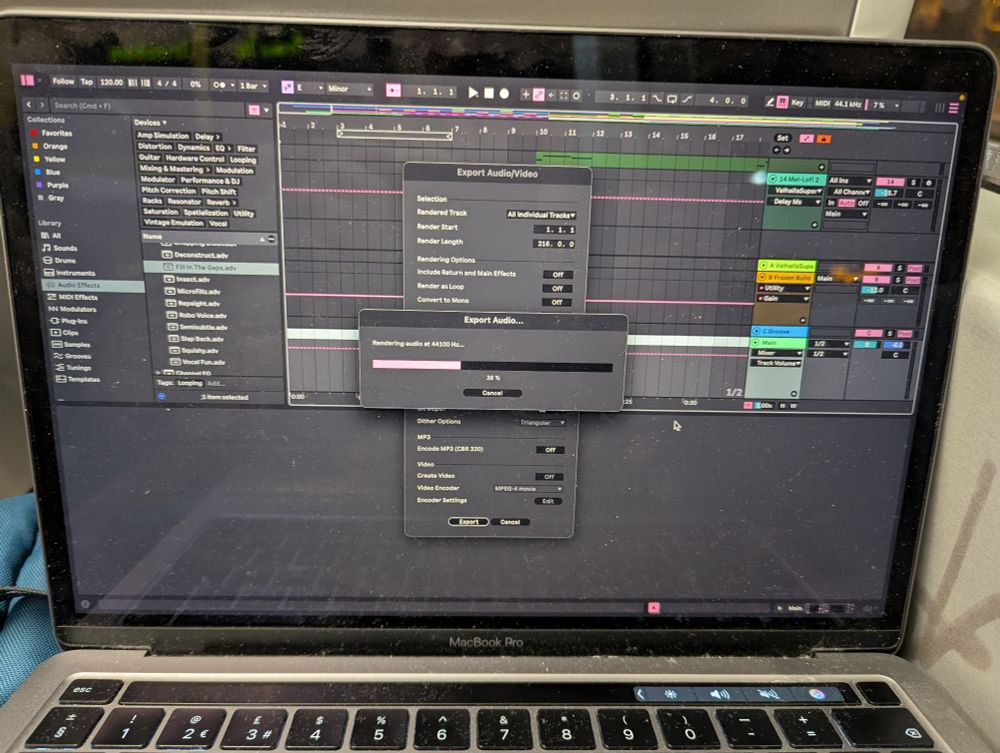 A laptop with Ableton open. The window shows a progress bar of the project exporting
