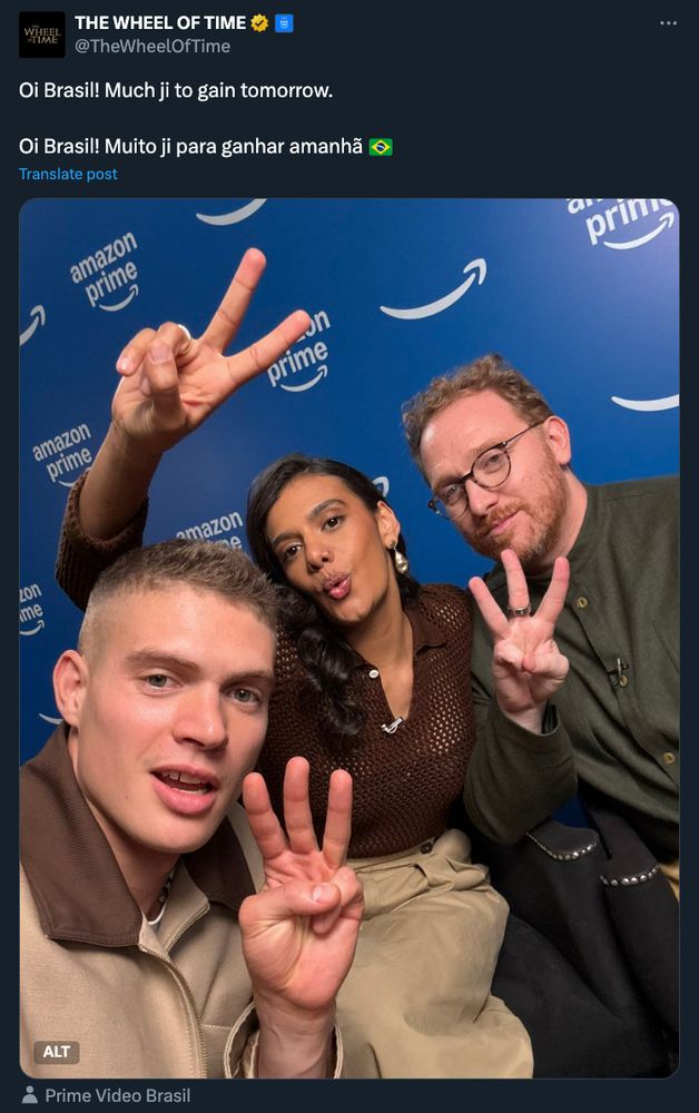 A tweet from the official The Wheel of Time account featuring a photo of actors Josha Stradowski, Madeleine Madden, and showrunner Rafe Judkins at CCXP24 in Brazil. The caption reads: ‘Oi Brasil! Much ji to gain tomorrow. Oi Brasil! Muito ji para ganhar amanhã 🇧🇷.’ In the photo, all three are posing in front of a blue background with Amazon Prime branding. Josha is in the foreground holding up three fingers, Madeleine is making a playful expression while holding up two fingers, and Rafe is smiling with three fingers raised, referencing Season 3 of The Wheel of Time. The tweet is addressed to Brazilian fans, hinting at upcoming news.