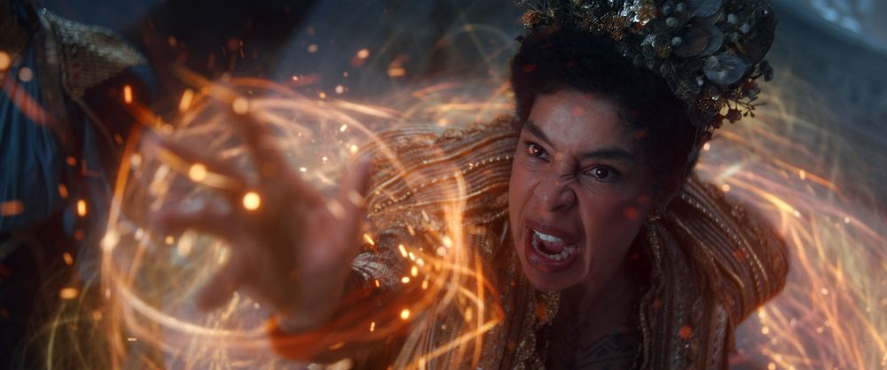 The image depicts Sophie Okonedo as Siuan Sanche, the Amyrlin Seat, channeling the One Power in Season 3 of The Wheel of Time. Dressed in opulent, gold-embroidered robes and wearing an elaborate crown-like headpiece, Siuan exudes authority and power. Her expression is fierce and focused as she extends her hand, commanding glowing, fiery threads of the One Power that swirl dynamically around her. 