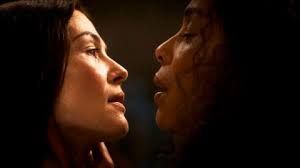 Rosamund Pike as Moiraine Damodred and Sophie Okonedo as Siuan Sanche share a close and intense moment, their faces nearly touching, conveying deep emotion and connection in a dimly lit setting.

