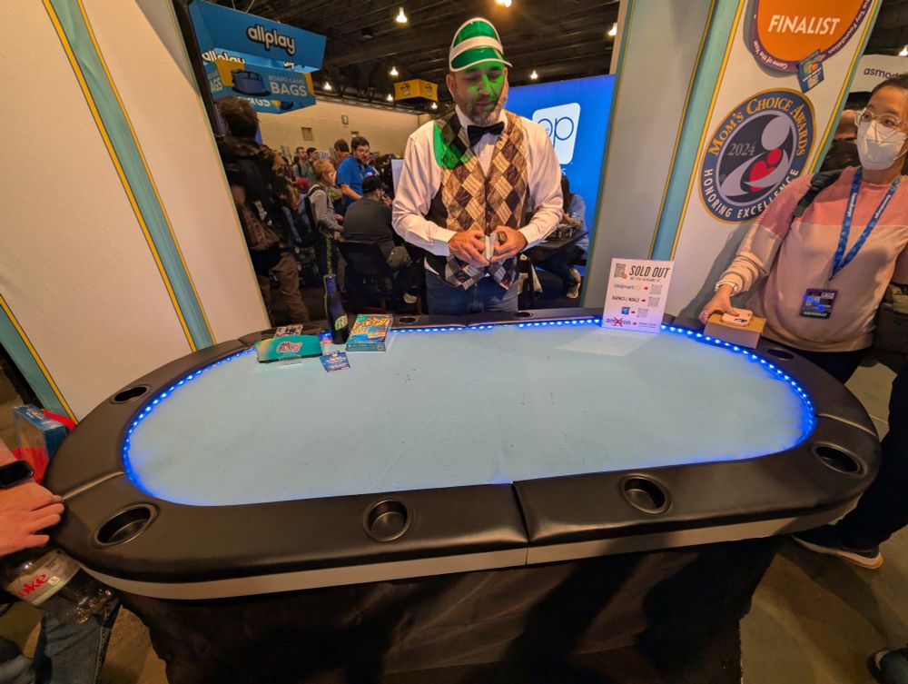 Photo of an exhibitor at PAX Unplugged showing off Flip7 at a poker table dressed as a casino dealer 