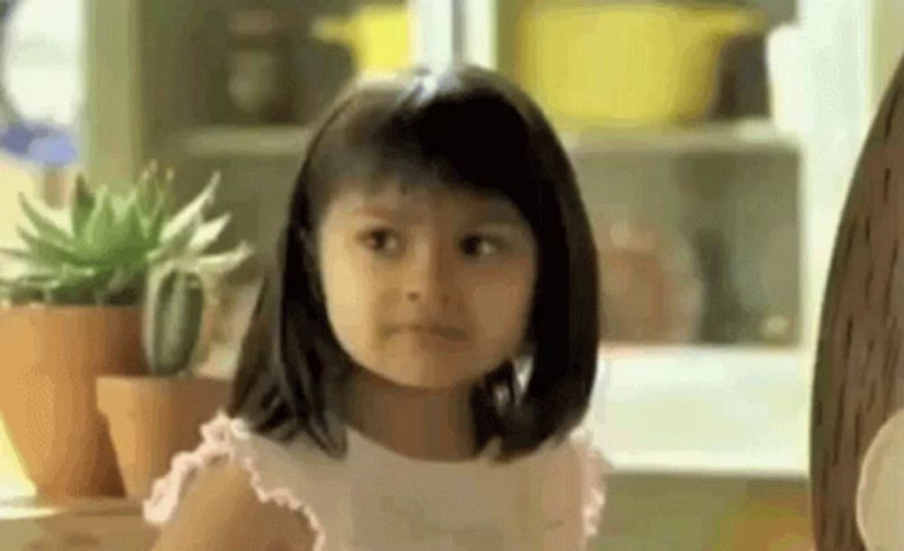 a little girl is making a funny face while sitting in front of potted plants .