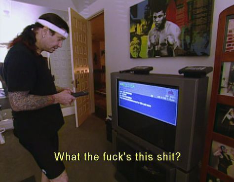 Ozzy com uma faixa de cabelo na testa, olhando pra uma tv com o controle remoto na mão falando “What the fuck’s this shit?”
