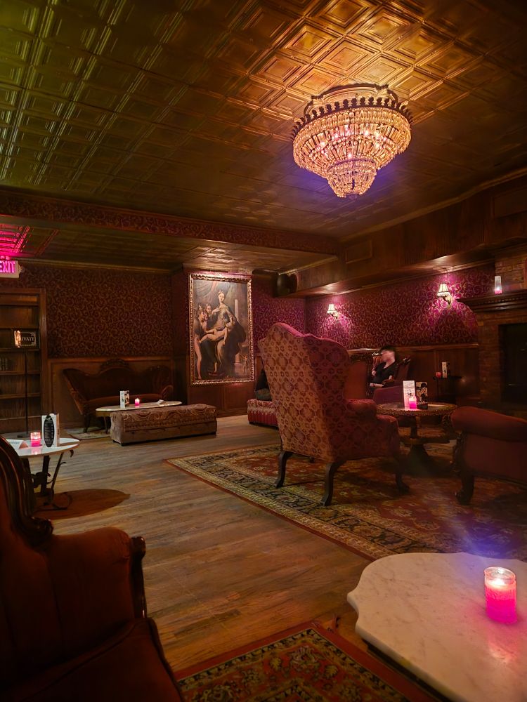 Foto de um speakesy chamado Blind Barber em Nova Yorke, uma sala com moveis antigos, lustres, quadros e paredes que também parecem de uma época passada