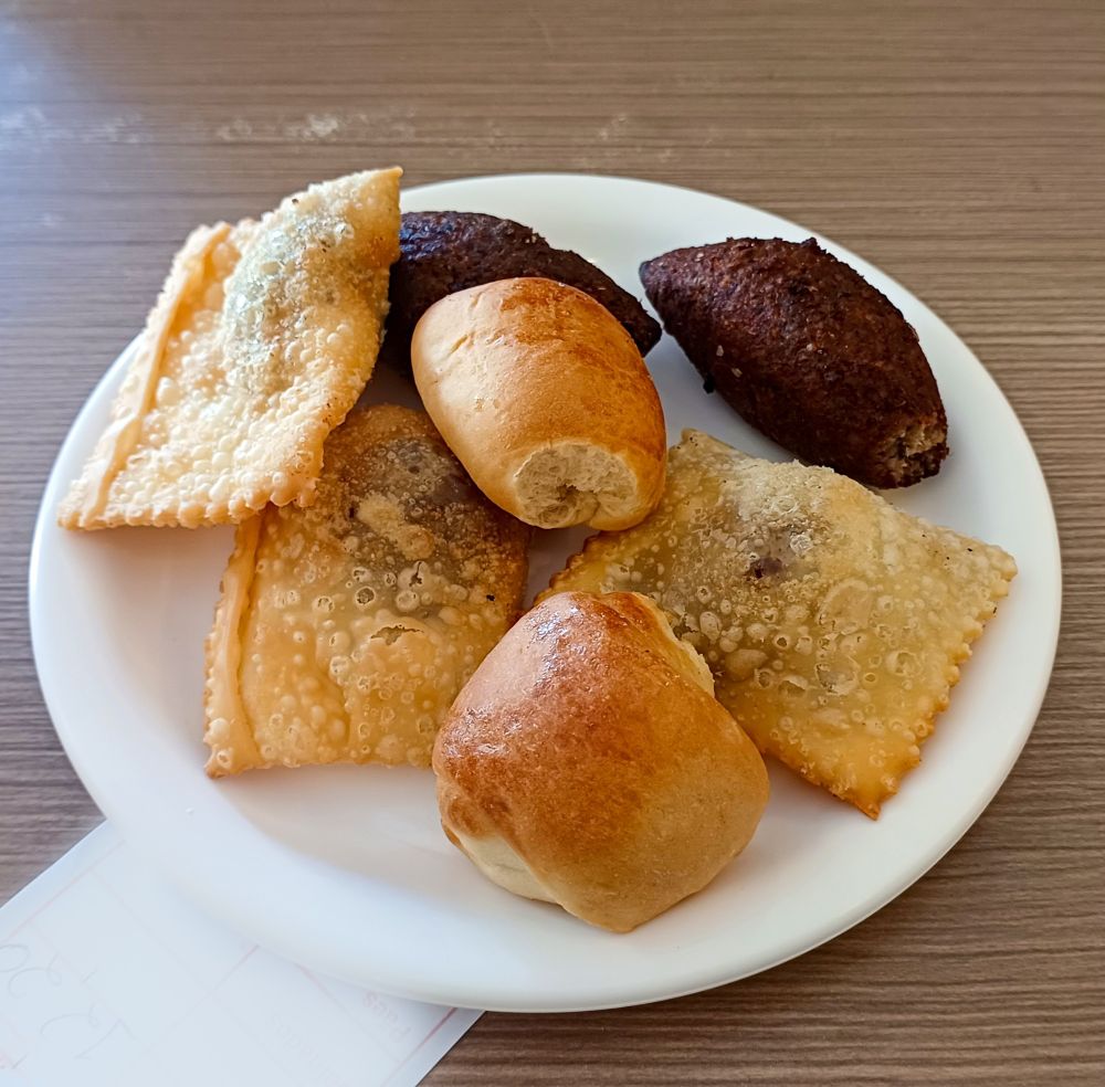 Imagem mostrando um prato branco com alguns mini salgados de festa: enroladinho, mini pastel frito, mini quibes. 