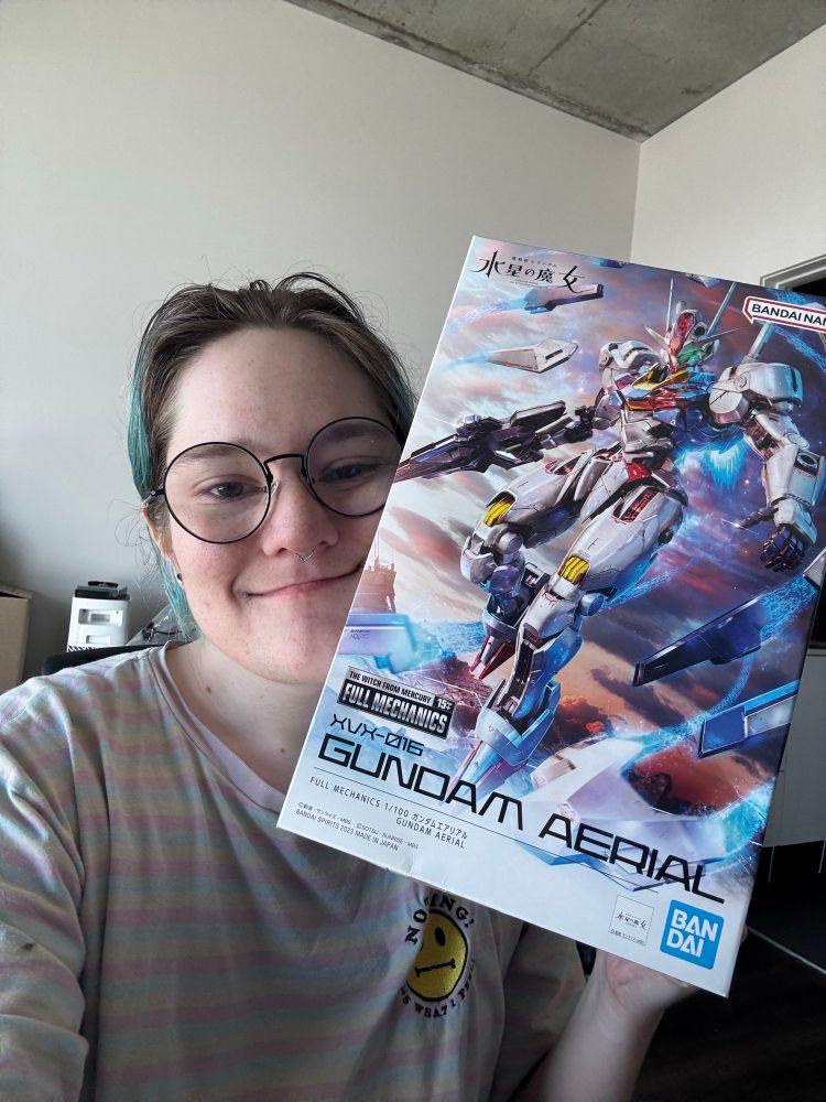jaiden posing with a box for a model kit for Aerial from Witch from Mercury