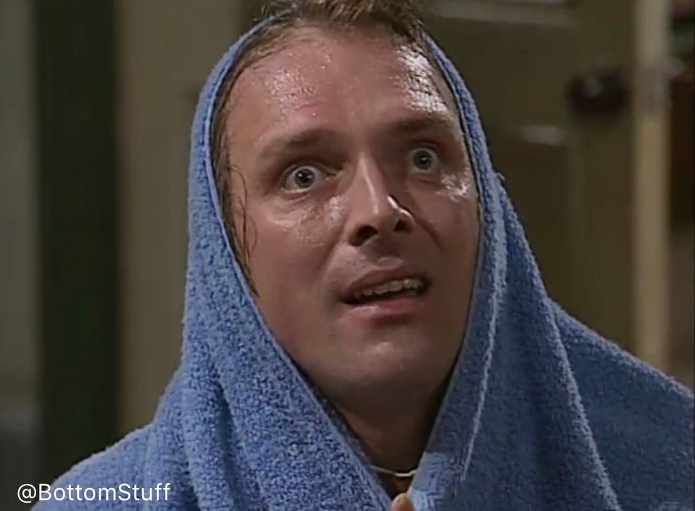 Rik Mayall as Richie Richard with a blue towel over his head. He looks to the distance in a million-yard-stare in the realisation that he's a virgin on Christmas Day. 