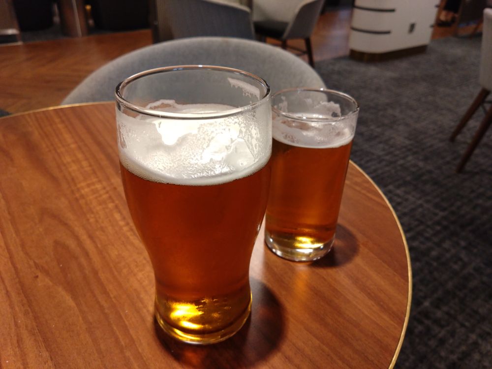 One pint and one half pint glass of beer sits atop a wood-effect round table. 