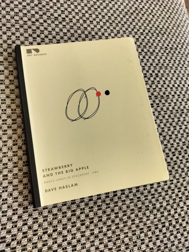 Strawberry and the Big Apple, Grace Jones in Stockport, 1080, by Dave Haslam.

In ‘Strawberry and the Big Apple’, the eighth short-format book in his acclaimed Art Decades series, Dave Haslam explains a seemingly unlikely scenario: the day in November 1980 when Grace Jones – a spectacularly glamorous jet-setting singer living and working in Paris and New York, and recording in the Bahamas – pays a visit to Stockport (a post-industrial town seven miles south of Manchester, with crumbling infrastructure and rising unemployment). Her quest that day? To meet A Certain Ratio, a group then signed to Factory Records.
This tale of worlds colliding includes Tony Wilson’s fascination with New York; an intriguing portrait of the early life of Grace Jones; a twist in the tale, and more than a couple of mysteries; plus walk-on parts for 10cc, Robert De Niro and Jerry Hall.
