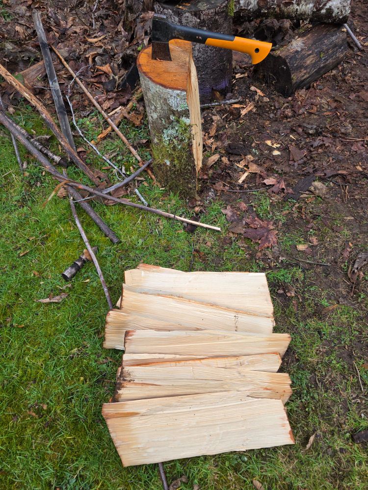 A log, split in half with the axe resting in the top. Next to the half-log, a pile of split wood from the other half of the log. 