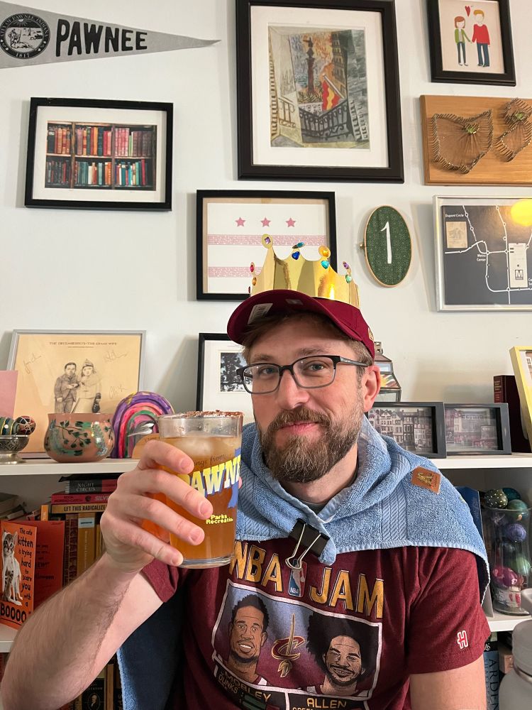 My smokeshow husband in a towel like a cape and a paper crown, holding a brunch beverage