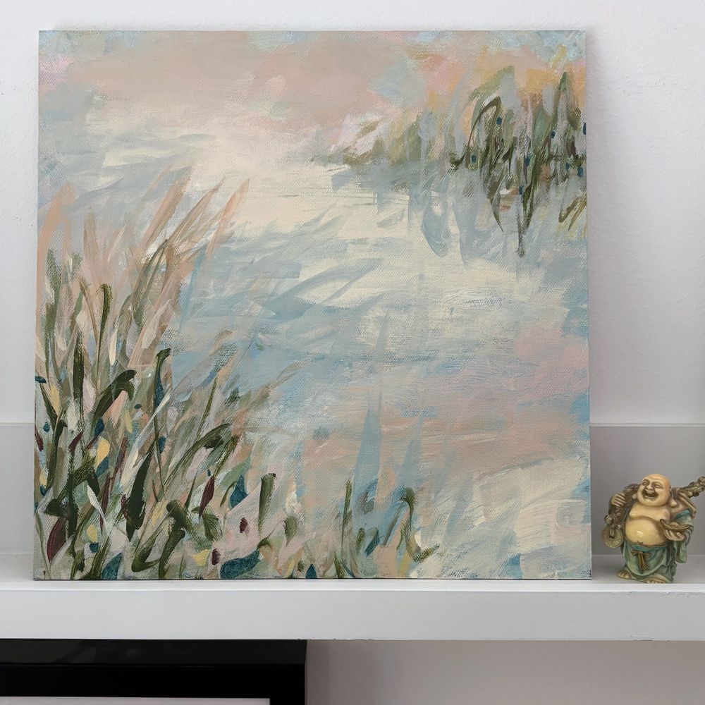 A small abstract painting sitting on a shelf next to a Buddha figurine. The painting shows expressive calligraphic marks in various greens and peach on a soft blue-gray and cream ground suggesting a landscape or marsh scene.