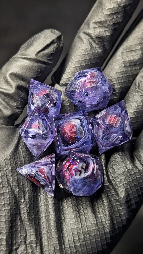 A black gloved hand holds a purple set in their palm. You can see glitter, white swirls, black flakes and a red blob peeking through the swirls, like planets emerging from the mists.