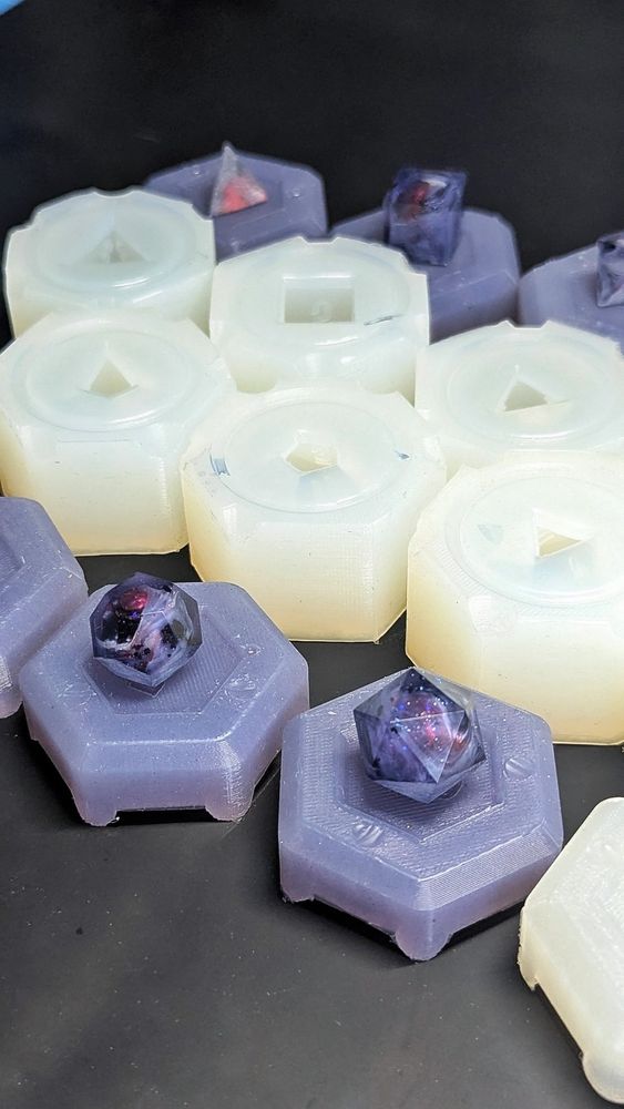 You see single dice molds in two rows. Beides them are the mold lids in a dusty purple. On top of each lid sits a purple blank with white wisps surround red orbs.