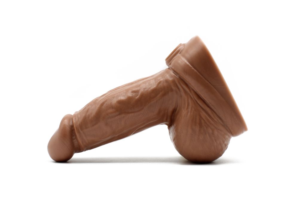 Daddy Dutch Dildo viewed from the side. It has a scooped head, a thick girthy shaft with veins, a HUGE pair of balls, and a belt detail wrapped around under the balls.