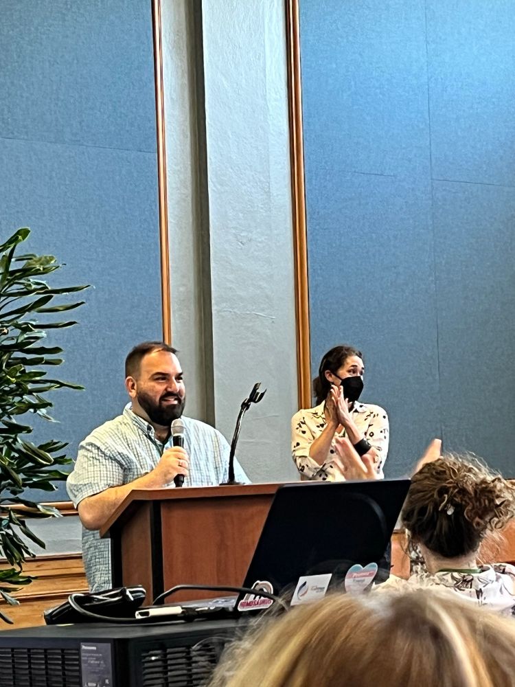 Patrick Thomas speaks into a microphone in front of an auditorium. 