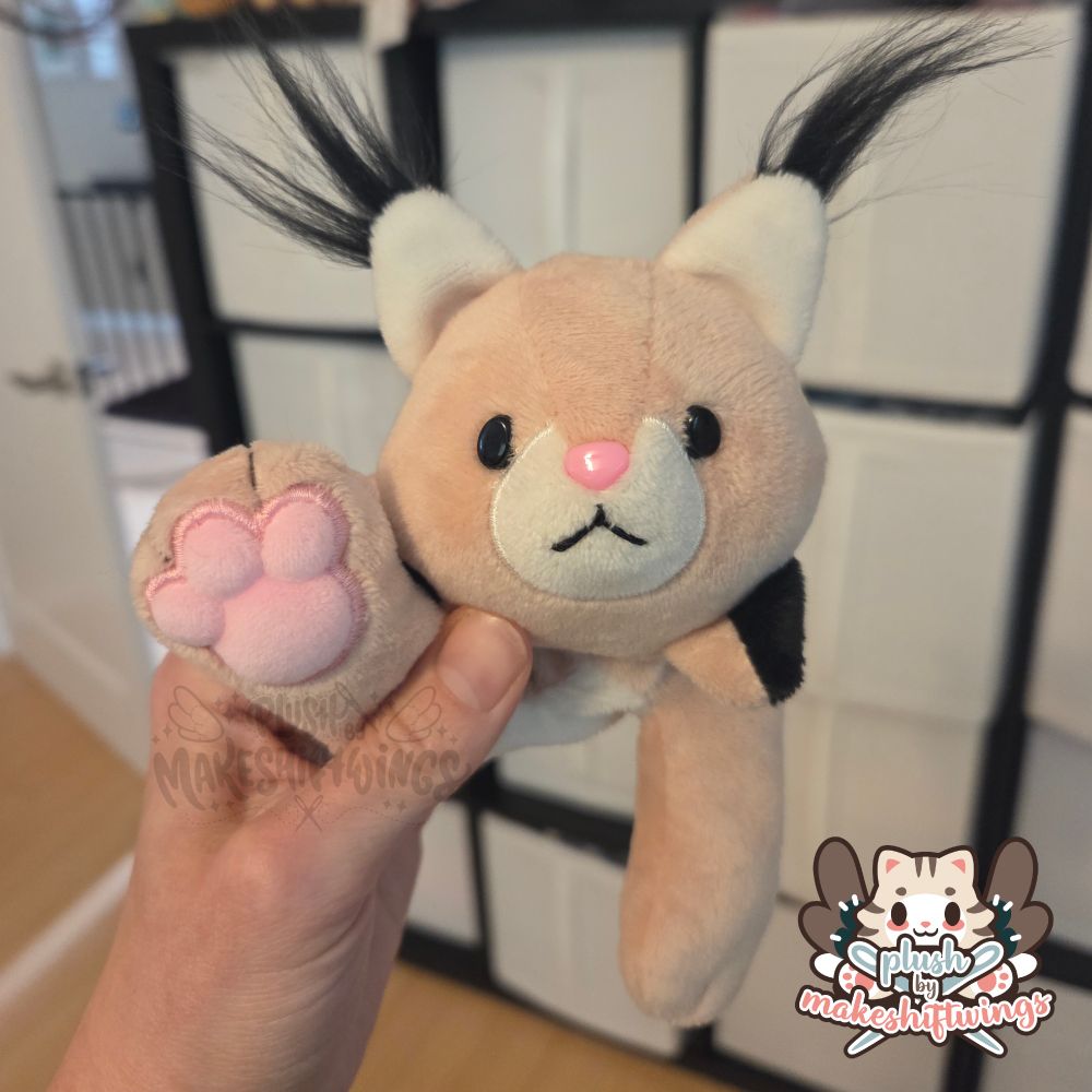 A beanie baby style plush of a lynx. Its paw is being held up showing very large squishy pink paw pads