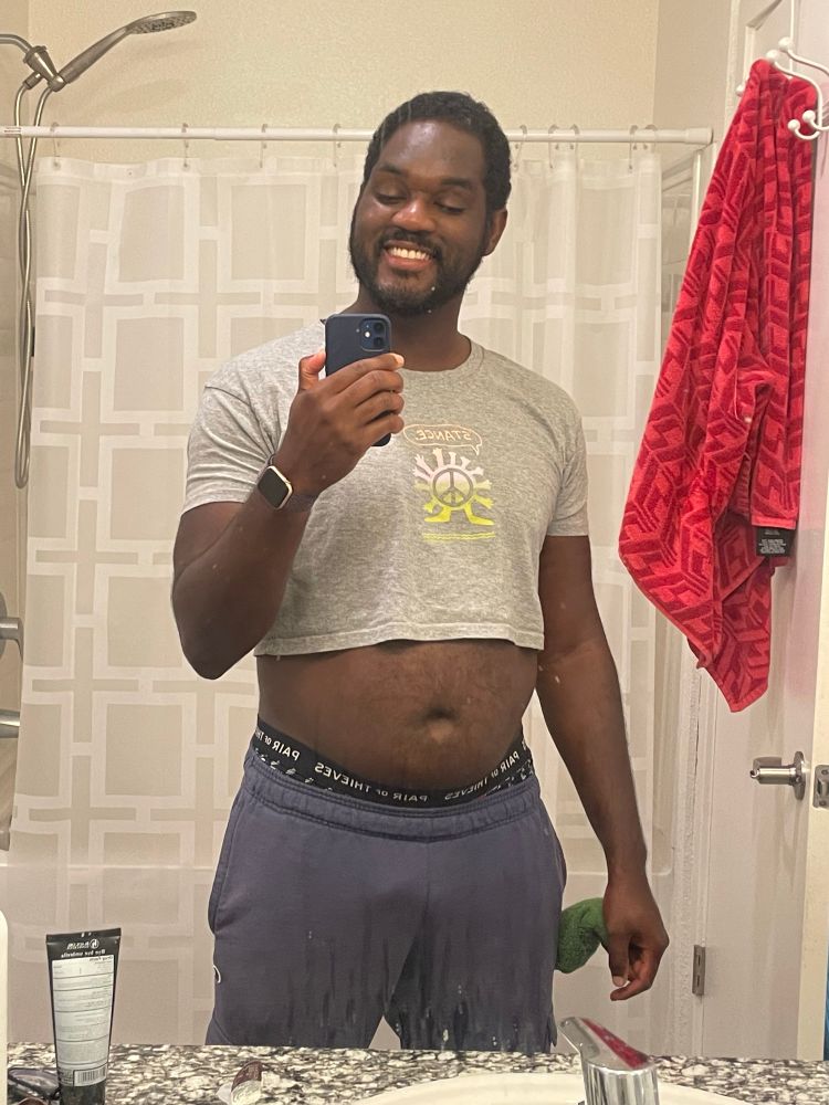 Black man wearing crop top smiling in mirror