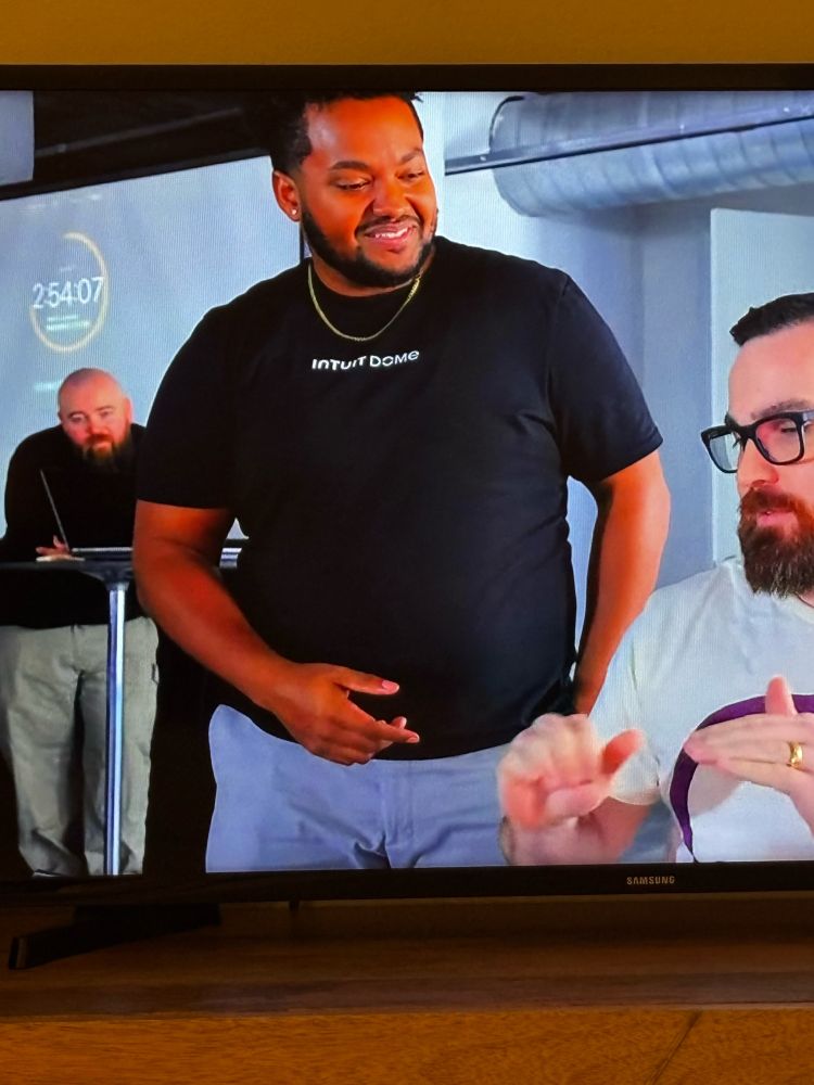 Still from the e-commerce edition of Web Dev Challenge in Houston. Robbie and Jordan collaborating in the foreground, Jason in the background, listening in. 