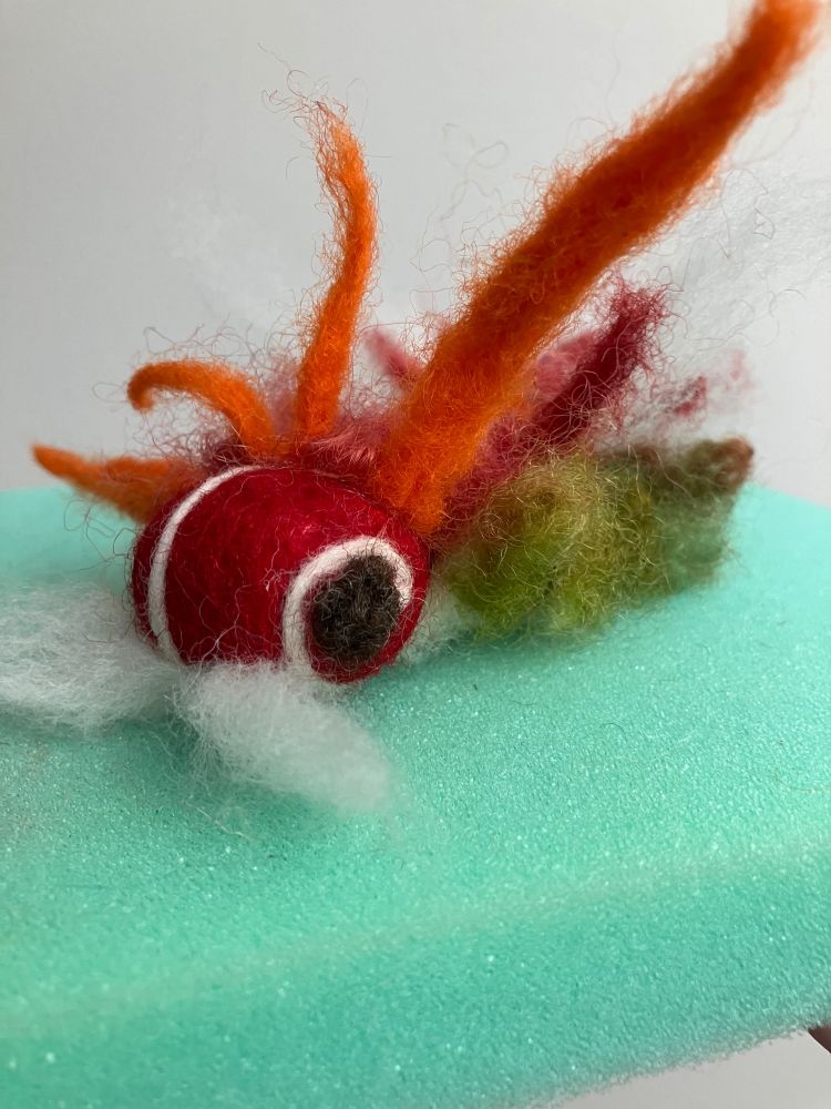 Red, orange, green, and white needle felted caterpillar with a white mustache