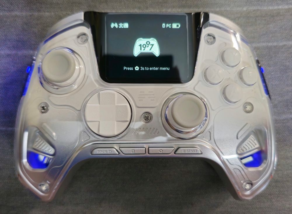 Straight down shot of the controller, showing better the transparent top which allows one to see the vibration motor weights. The screen is now in English and the controller paired and idle. It has an outline of a controller with a stylized "1997" inside it.