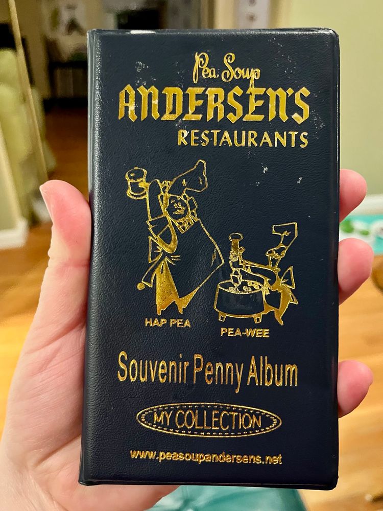 Hand holding a smashed penny album with the mascots two mascots of Pea Soup Andersens
