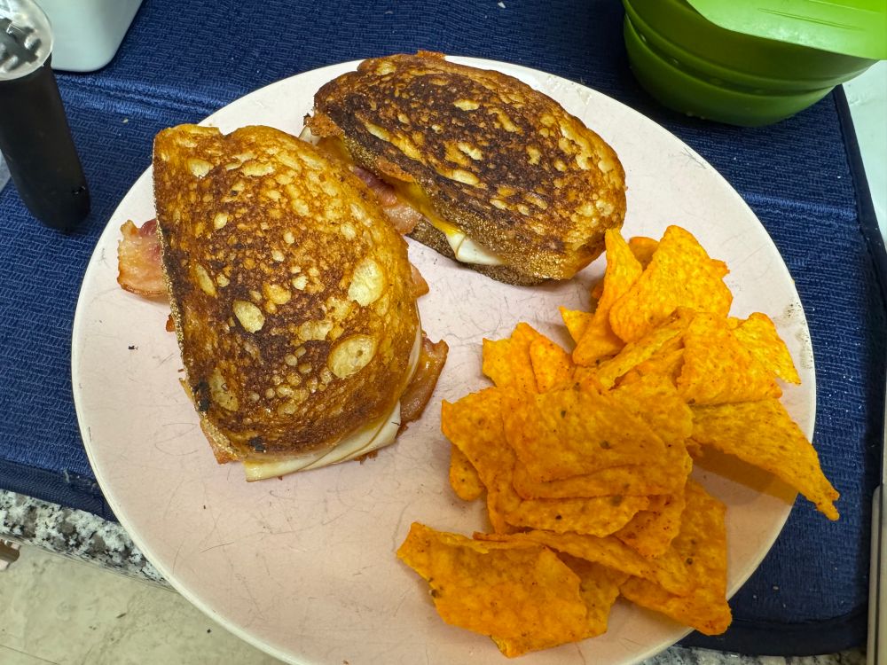 Two griddled chicken, bacon, and cheese sandwiches and a side of Doritos on a pink plate in my kitchen 