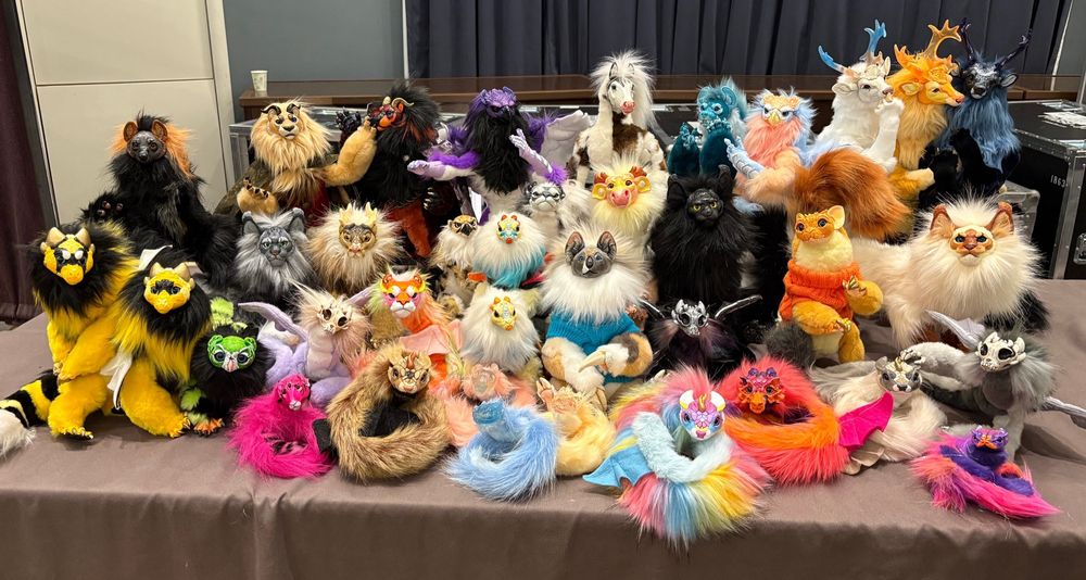 A large number of ball jointed art dolls on a table. There is a mix of anthro, feral and even snake styled creatures in a variety of furs and painted resin faces. 