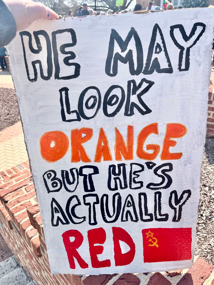 My protest sign, painted in black bubble letters, which reads, “HE MAY LOOK ORANGE (painted in the color orange) BUT HE’S ACTUALLY RED (painted in the color red)”, followed by a painting of a (red) Soviet flag