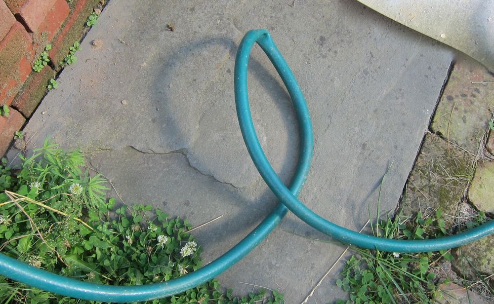 Green garden hose that is bent sharply enough to form a kink (blockage)