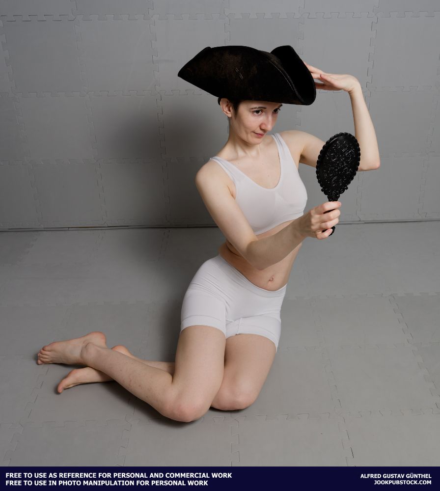A drawing reference photo of a model wearing form fitting sports wear, sitting on the floor, wearing a pirate hat and locking into a hand mirror.