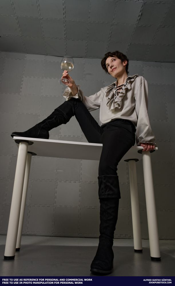 A drawing reference photo of a model wearing a dress shirt and black pants, sitting on a table and holding a wine glass.