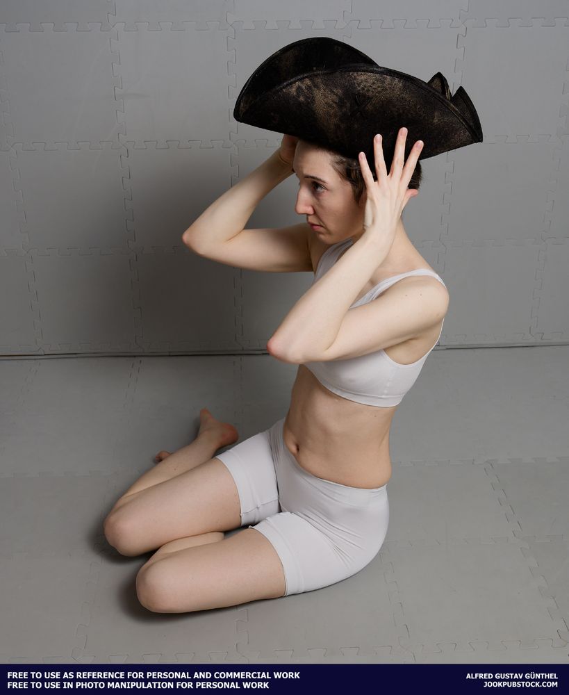 A drawing reference photo of a model wearing form fitting sports wear, sitting on the floor, and putting on a pirate hat.