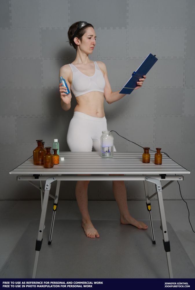 A drawing reference photo of a model in form fitting sportswear standing at a table, looking at a clipboard, holding a flask.