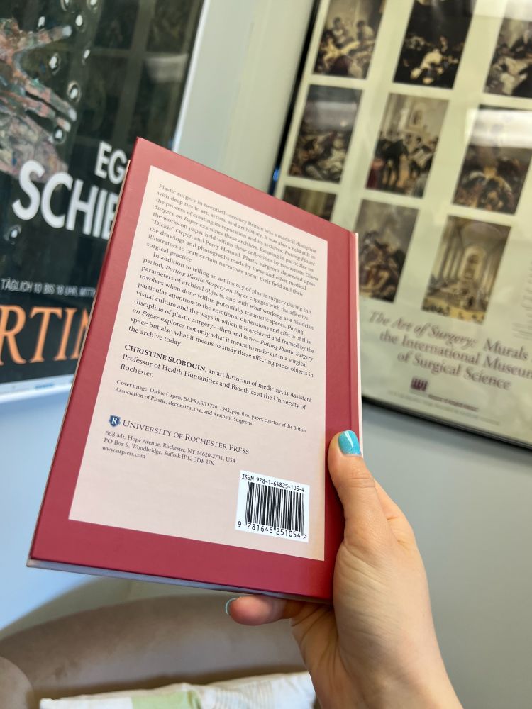 The back of the book, held in front of the same two framed posters. The text isn't super visible, but it includes the blurb of the book from the publisher's website, and the bio of the author, Christine Slobogin, as well as the press's logo and the barcode. The beige text box is outlined in dark red.